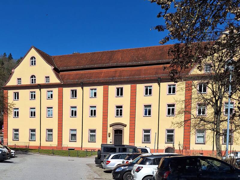 Großes Gebäude in gelb und orange mit drei Stockwerken und mehreren Dachgauben.