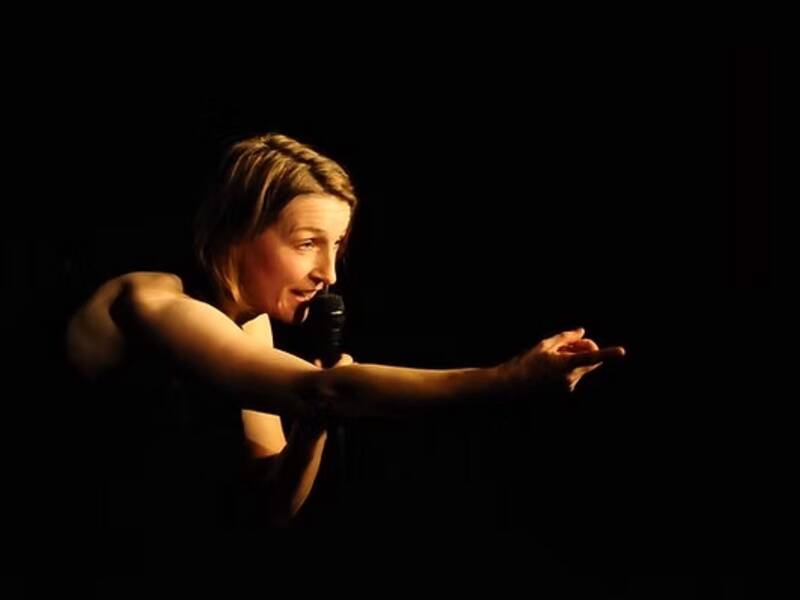 Frau die in ein Mikrofon singt, sie zeigt nach rechts, hier fliegt eine Patrone